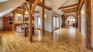 Ein geräumiges Loft mit freiliegenden Holzbalken, einem Essbereich mit Tisch und Stühlen und großen Fenstern für viel Tageslicht.