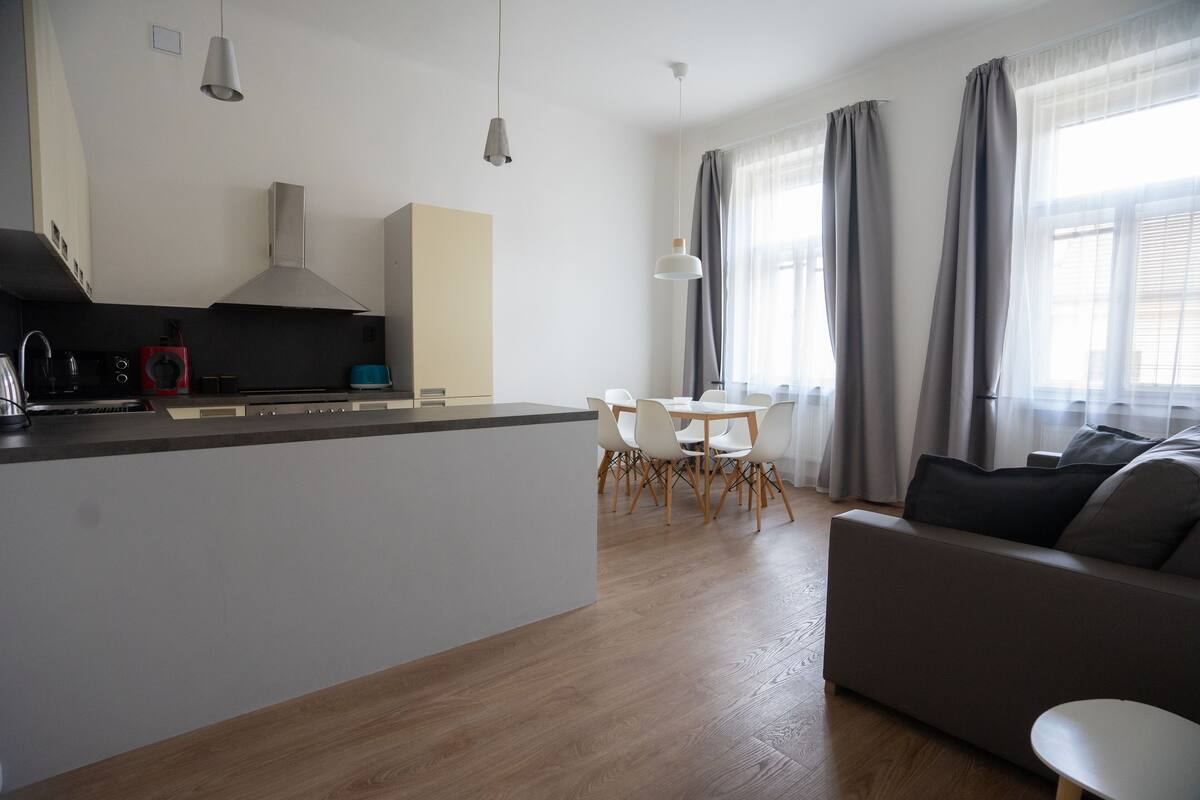 A modern kitchen with a central island, dining area with chairs, and a sofa.