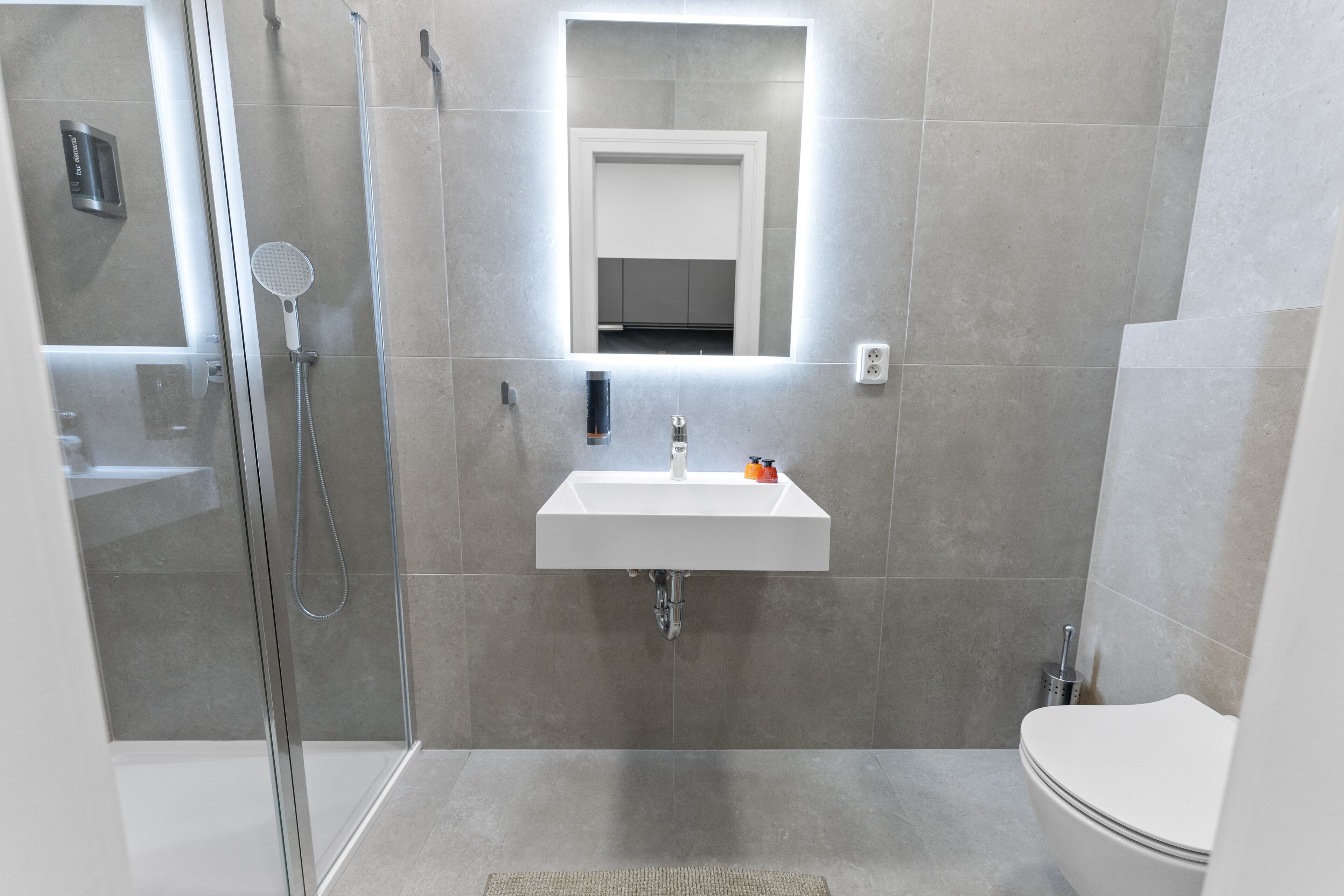 A modern bathroom with a glass shower enclosure, a white sink with a mirror above it, and a toilet.