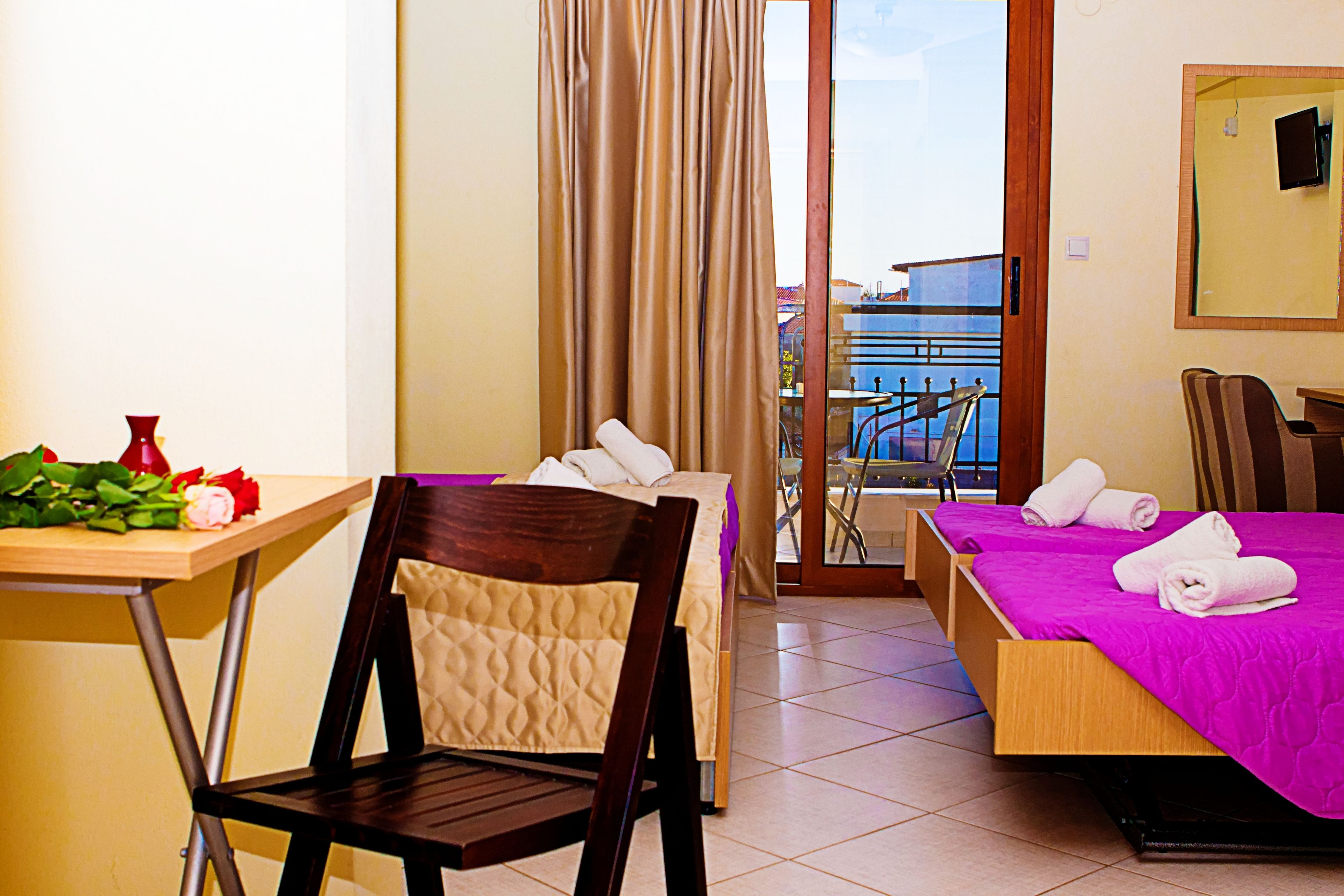 A hotel room with a bed, a chair, a table with flowers, and a view of the sea through a balcony.