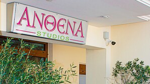 Une devanture de magasin avec une enseigne indiquant « ANOENA STUDIO'S ». Un grand pot de fleurs se trouve à droite de l'entrée.