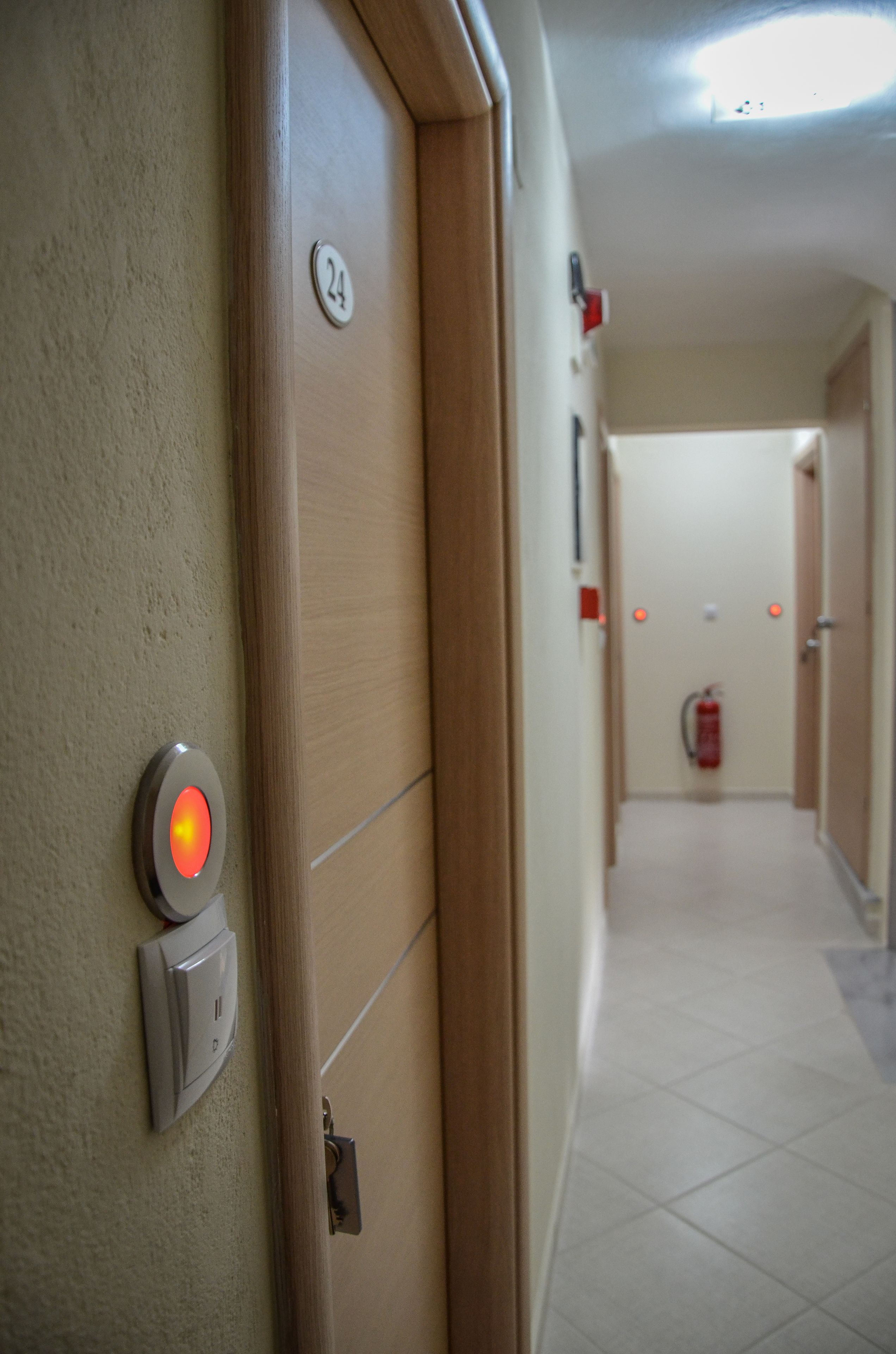 Un couloir d’hôtel avec une porte portant le numéro « 24 », une alarme incendie et, au loin, un extincteur.