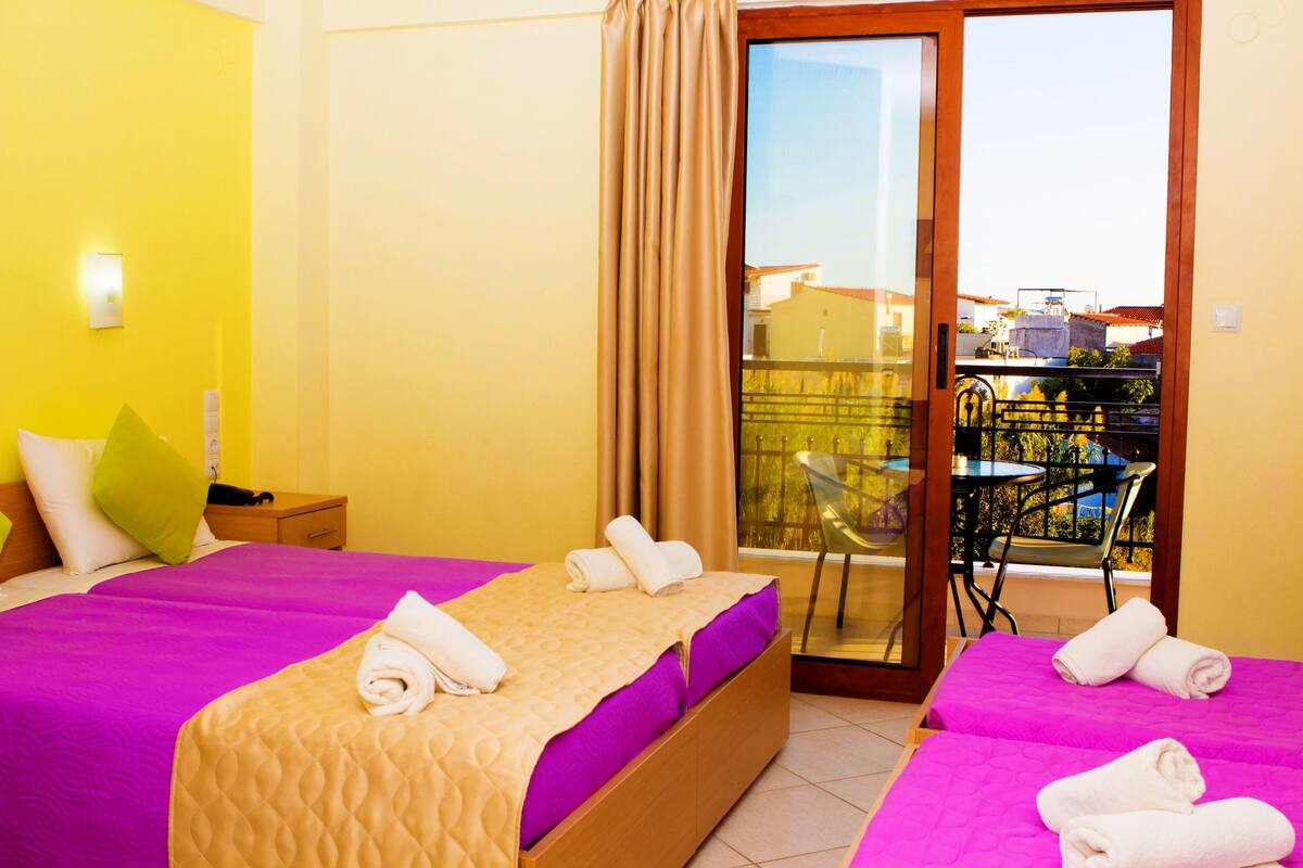 Een hotelkamer met twee bedden, een balkon met tafel en stoelen en uitzicht op de stad.