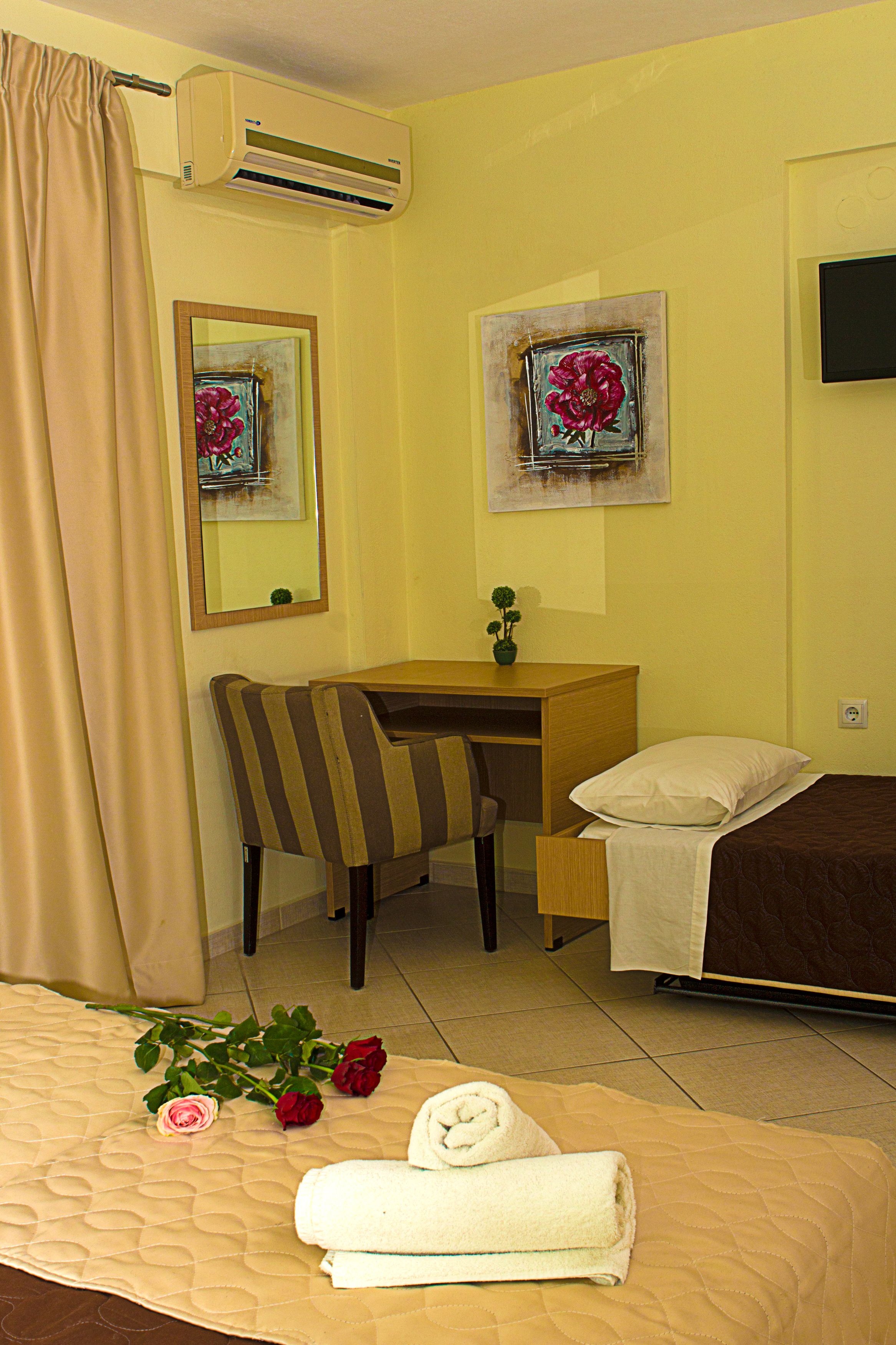 Habitación de hotel con cama, escritorio, silla, espejo, un cuadro y equipo de aire acondicionado.
