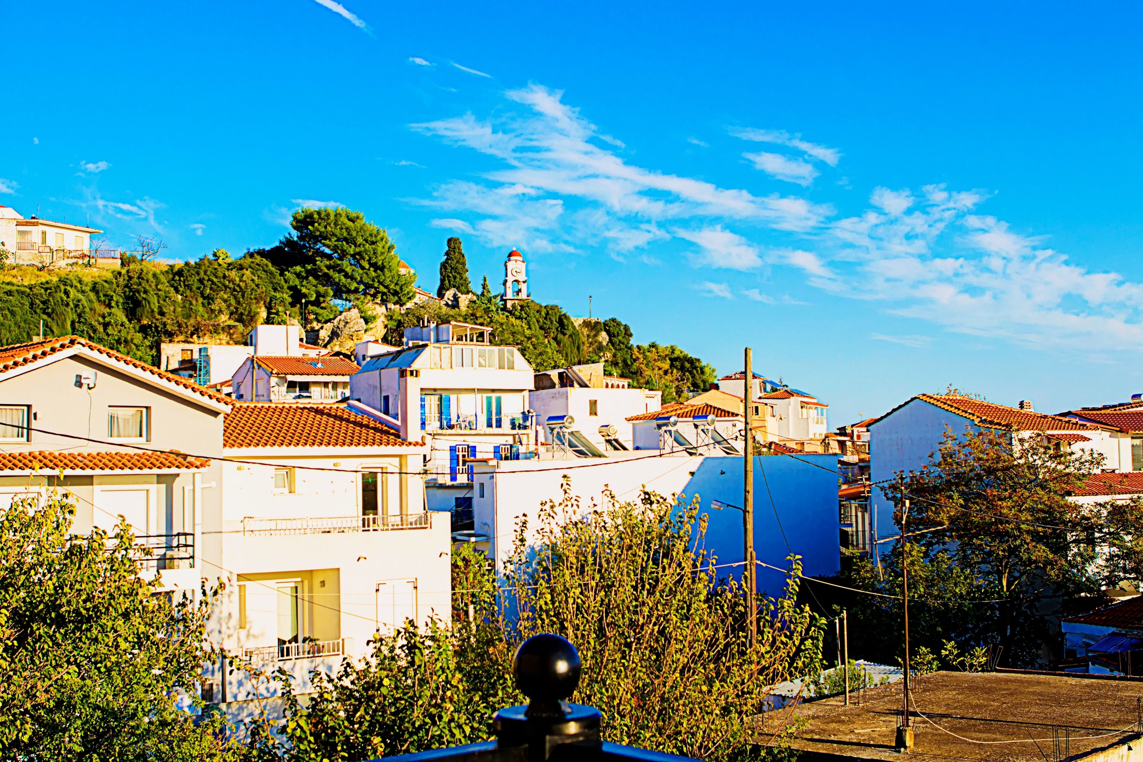 Un pueblo costero con edificios en una ladera, un faro destacado y un cielo azul despejado.