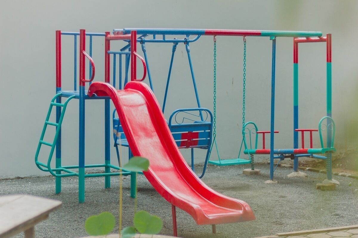 Un parque infantil con un tobogán rojo, columpios azules y rojos, y una estructura para escalar.