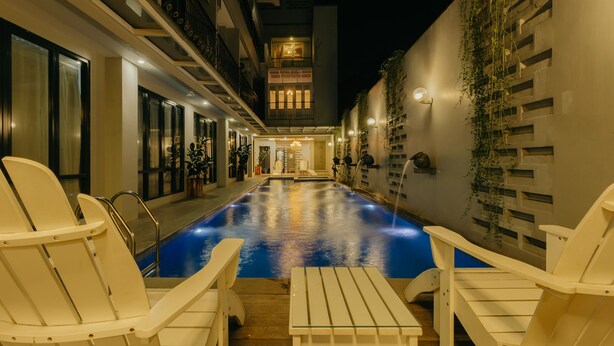 A pool area with white chairs and a table, surrounded by a building with balconies and windows. - Urbanest Inn House TB Simatupang (Jakarta)