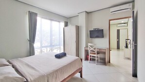 A hotel room with a bed, a desk, a chair, a TV, and an air conditioning unit. - Urbanest Inn House TB Simatupang (Jakarta)