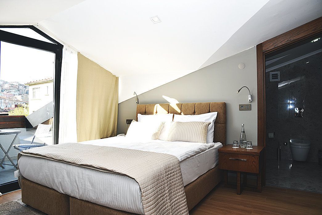 A bedroom with a large bed, a bedside table, a window with curtains, and a view of the city.