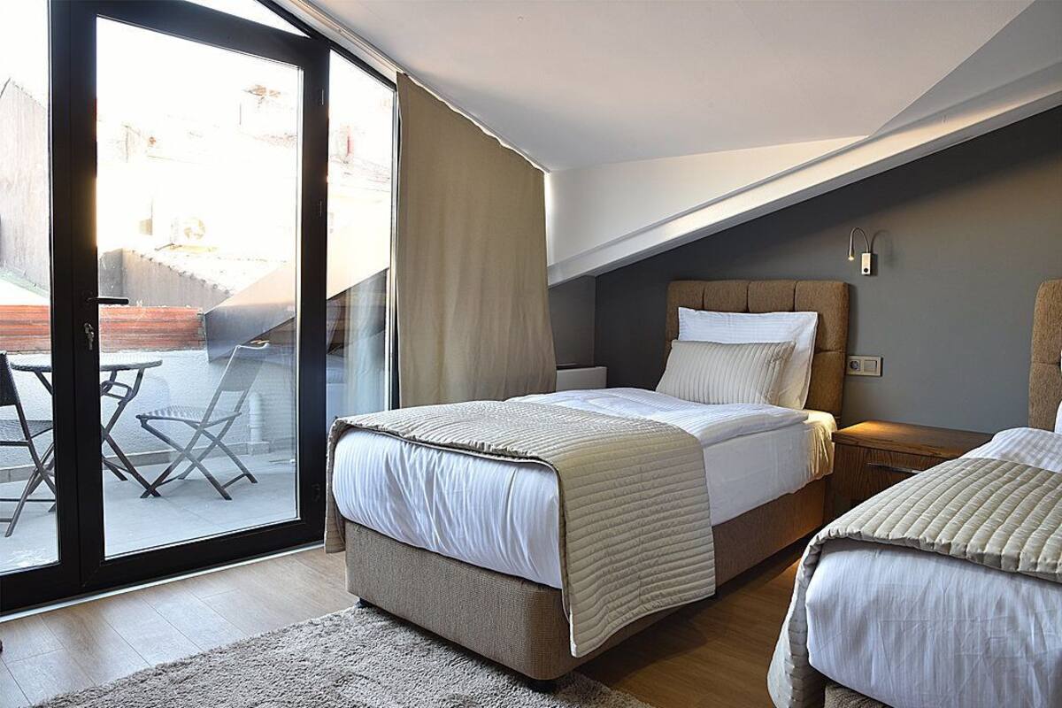 A bedroom with a bed, a nightstand, a window with curtains, and a view of the outside.
