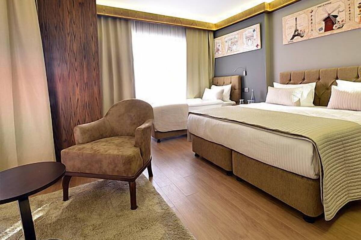A hotel room with a large bed, a chair, a small table, and a large window.