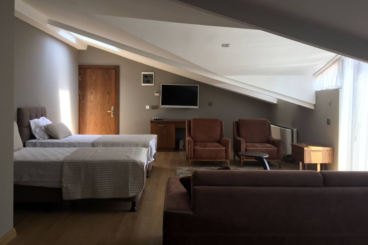 A modern loft bedroom with a large bed, a sofa, two armchairs, and a TV.