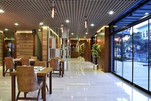 En modern hotellobby med en lång korridor, träbord och stolar samt stora fönster som ger utsikt över omgivningarna.