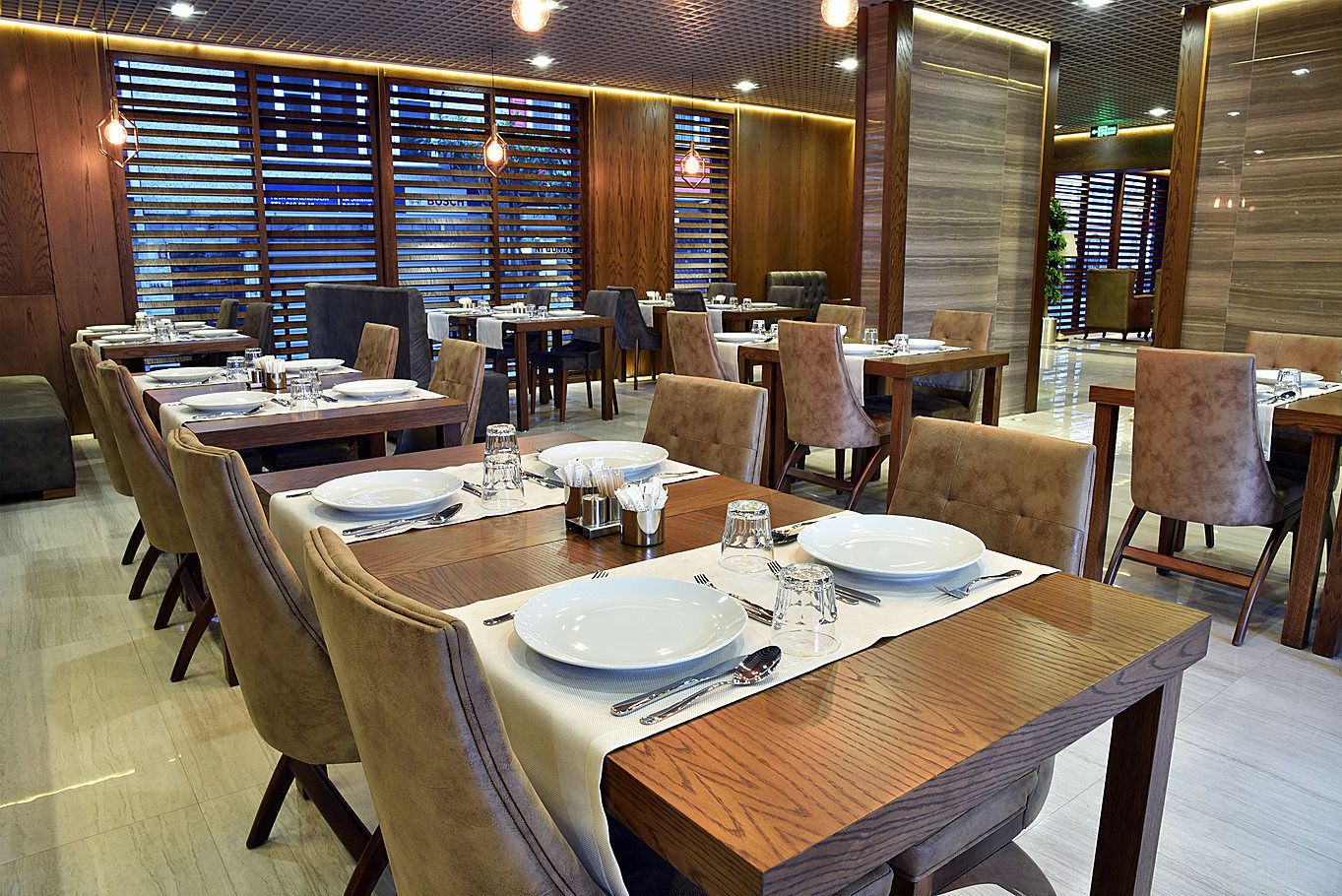 Un restaurante con varias mesas dispuestas, adornadas con platos blancos, cubiertos y vasos.