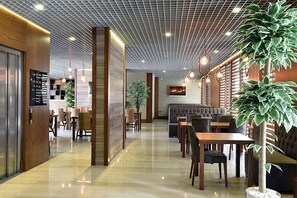Een modern restaurantinterieur met een plafond in rasterpatroon, houten details en een combinatie van zitplaatsen, waaronder tafels en hoekbanken.