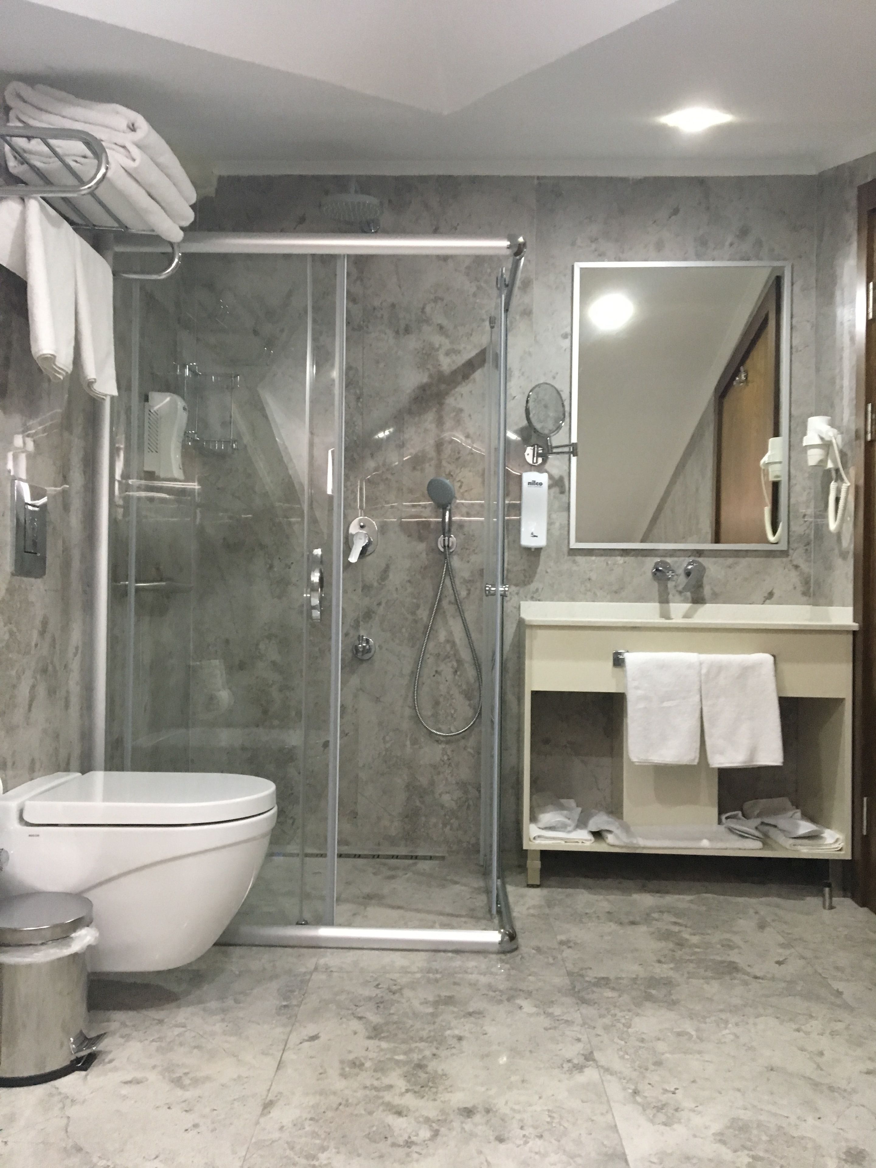 Un baño moderno con ducha envuelta en vidrio, inodoro blanco, tocador con espejo y barra para toallas.
