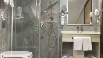 Un baño moderno con ducha envuelta en vidrio, inodoro blanco, tocador con espejo y barra para toallas.