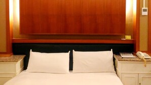 A hotel room with a large wooden headboard, two white pillows, a bedside table with a telephone, and a nightstand with a lamp. - Yachuan Hotel (Taipei)