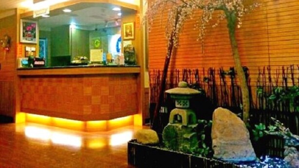 A reception area with a wooden reception desk, a green wall, and a decorative tree with white flowers. - Yachuan Hotel (Taipei)