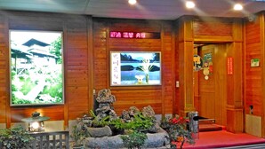 A reception area with wooden walls, a reception desk, a TV screen, and a stone garden. - Yachuan Hotel (Taipei)