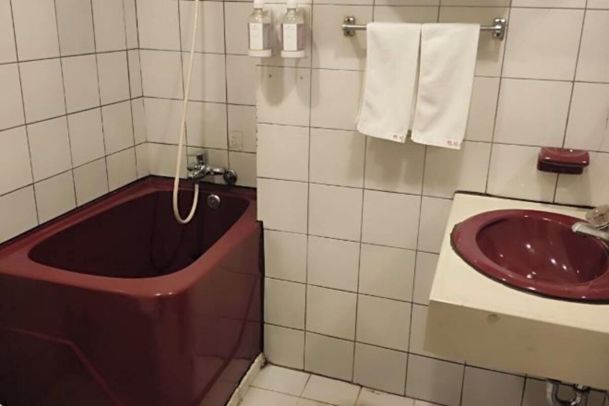 A bathroom with a red bathtub, a white sink, and two bottles of soap on the wall.