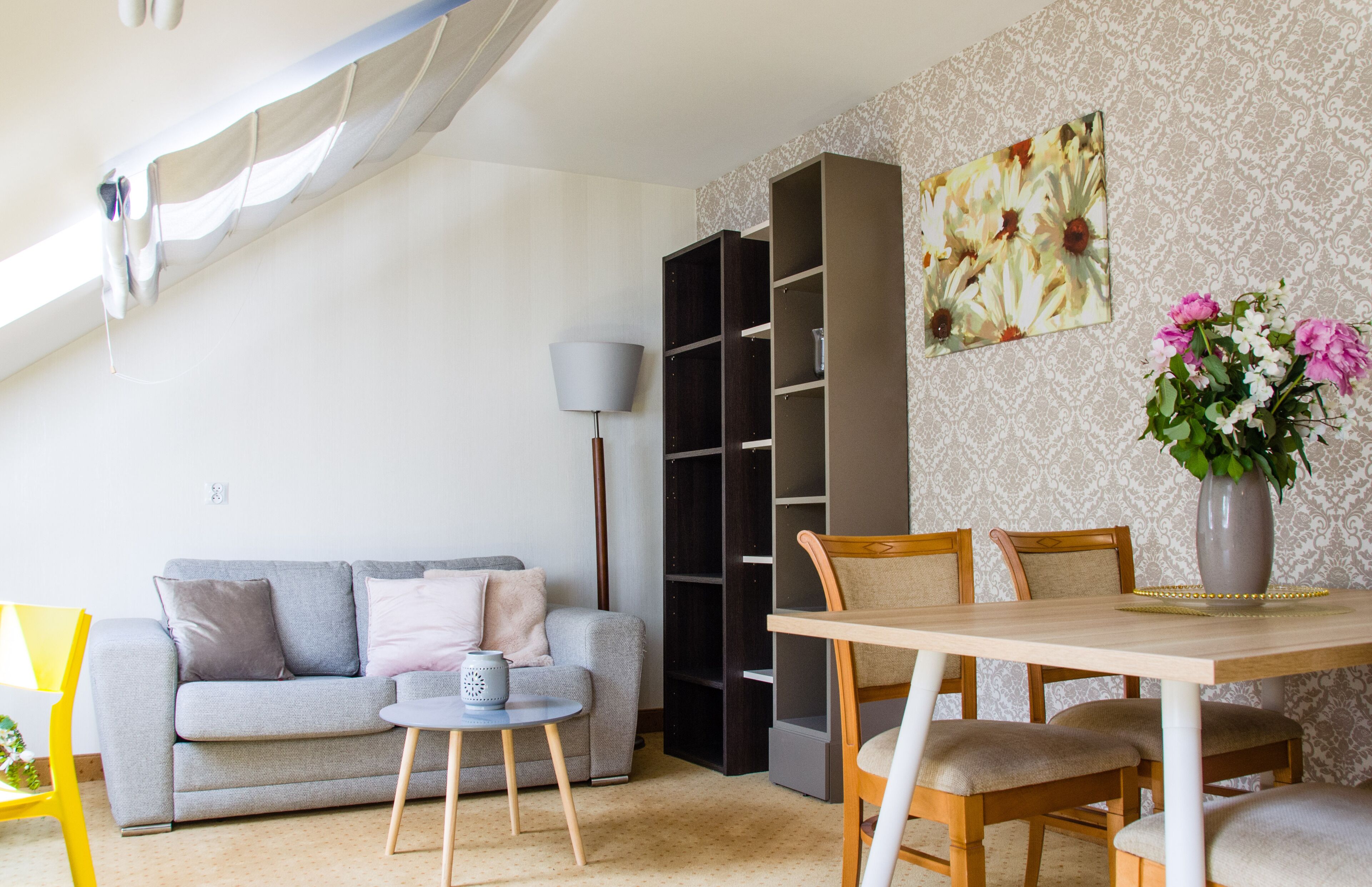 Una sala de estar con sofá, mesa de centro, estantería y mesa de comedor con sillas.