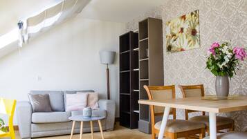 A living room with a sofa, a coffee table, a bookshelf, and a dining table with chairs.