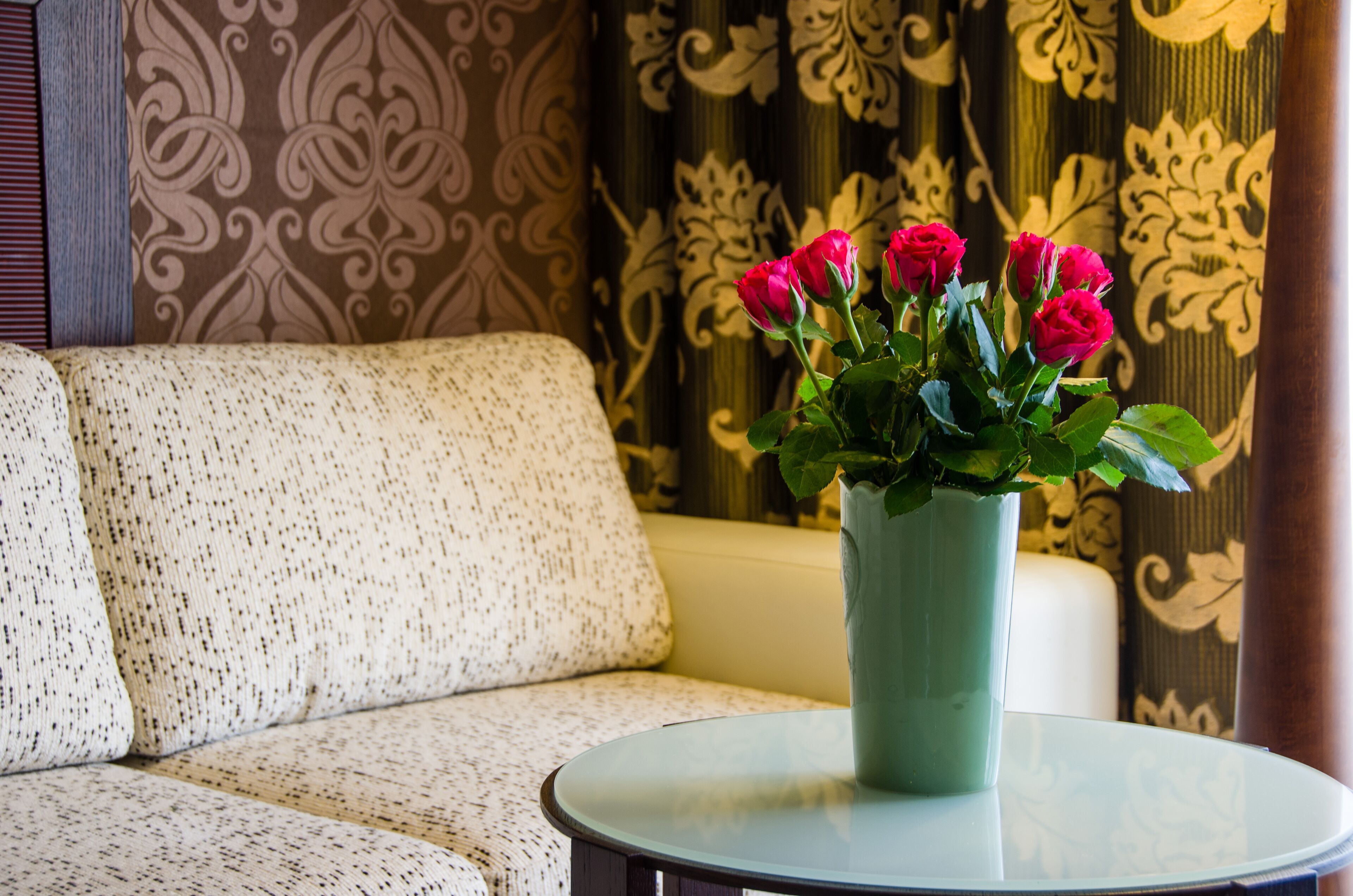 A room with a patterned sofa, a glass table, and a vase with flowers.
