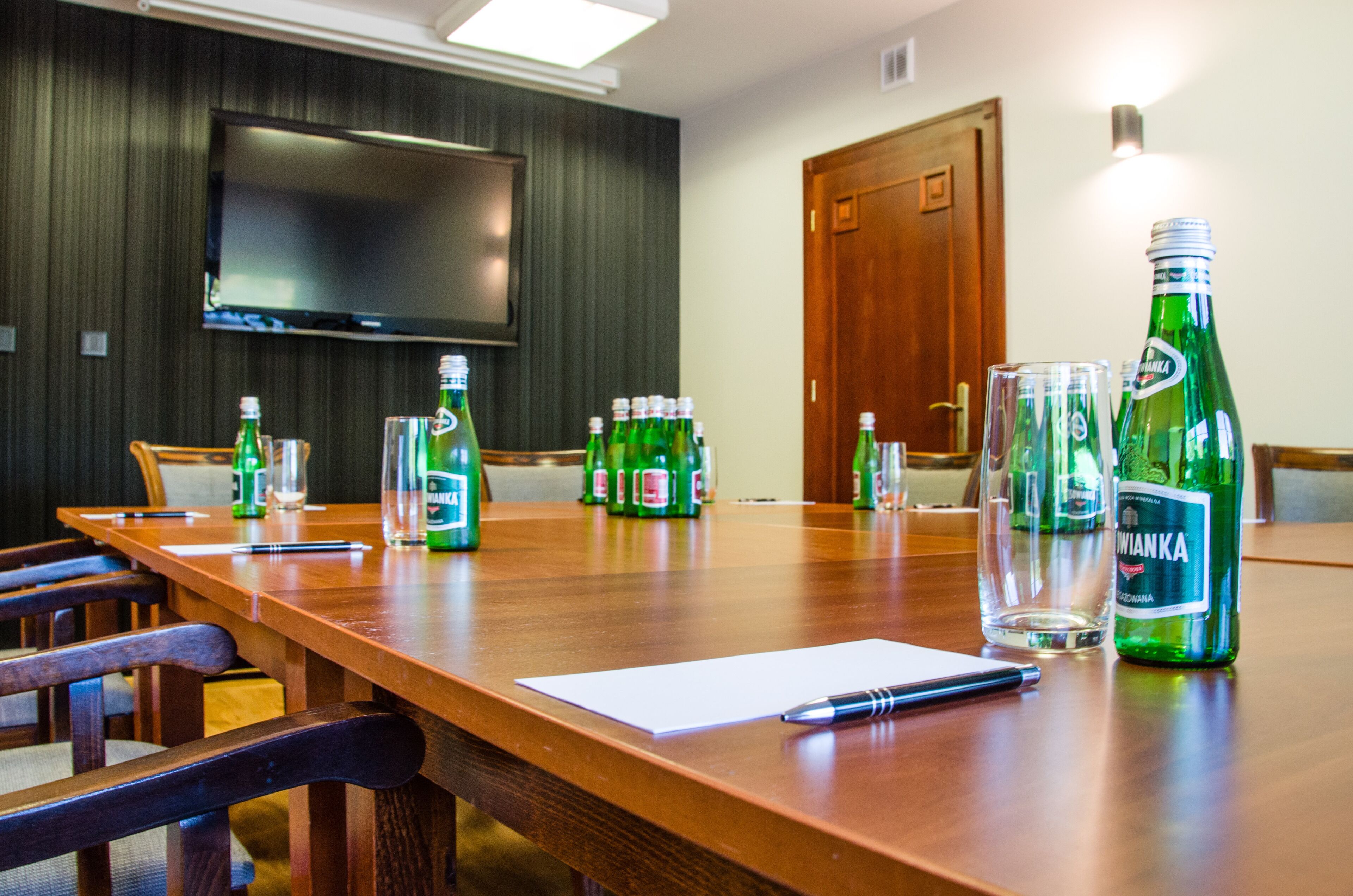 A conference room with a long wooden table, chairs, a television mounted on the wall, and several bottles of beer and glasses on the table.