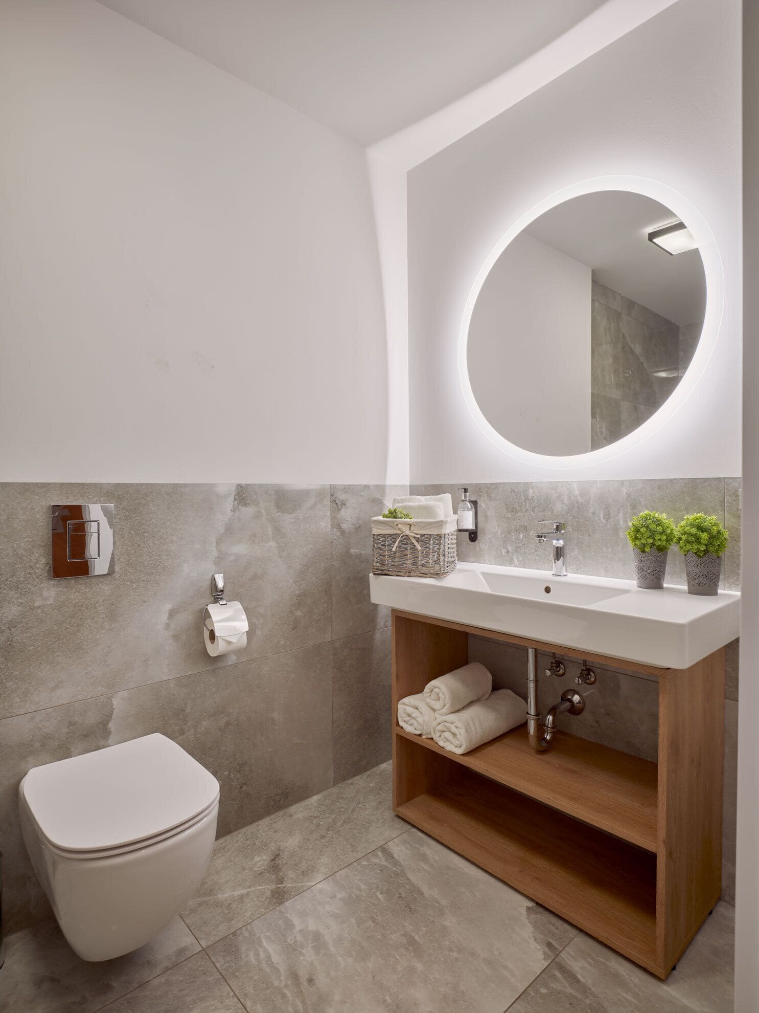 Et moderne badeværelse med et hvidt toilet, en trækommode med spejl og et håndvask.