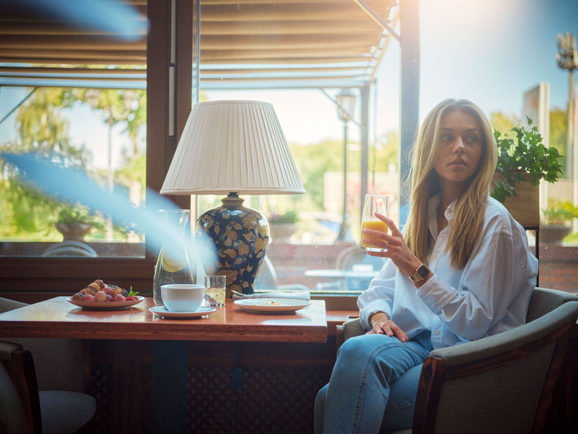 A person sitting at a table with a lamp, a glass of juice, and a plate of food.