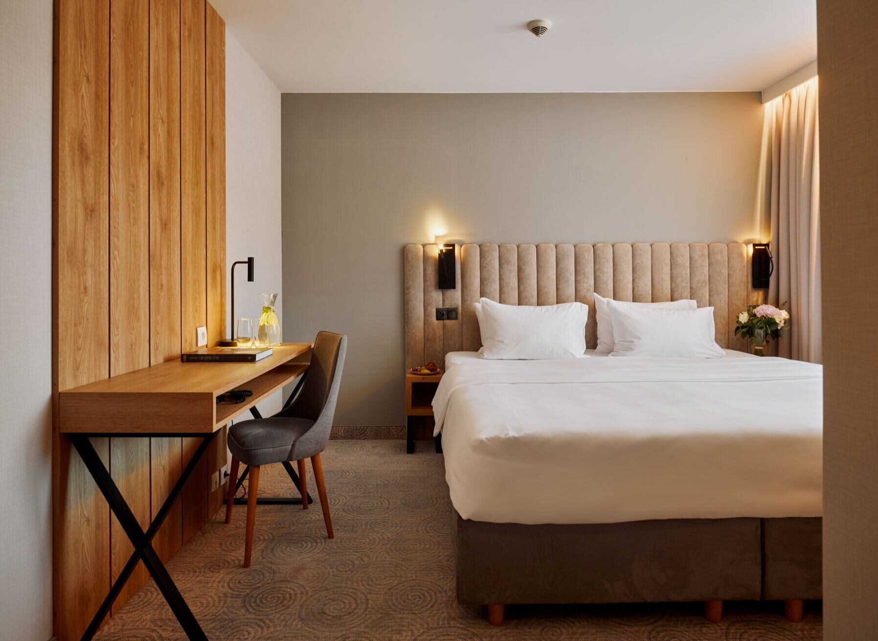 A hotel room with a bed, a desk, a chair, and a nightstand.