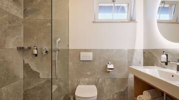 A modern bathroom with a glass-enclosed shower, a toilet, a sink with a mirror, and a window above the sink.