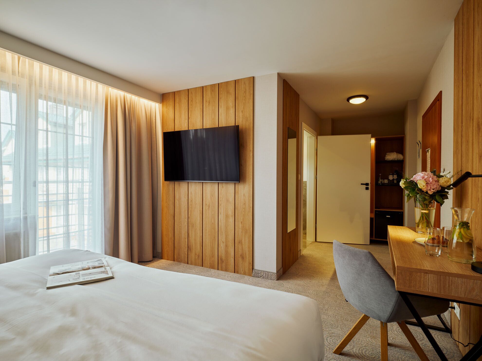 Une chambre d’hôtel dotée d’un grand lit, d’un bureau avec une chaise, d’un téléviseur à écran plat fixé au mur et donnant sur le couloir.
