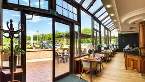 Un vestíbulo de hotel con ventanas amplias, una recepción y varias mesas y sillas.