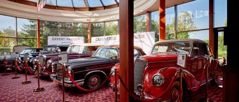 A museum interior with vintage cars on display, glass ceiling, and informational signs.