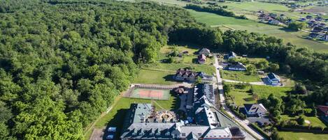 Vista aérea de un extenso complejo de edificios con varias construcciones, rodeado de un bosque denso y campos abiertos.