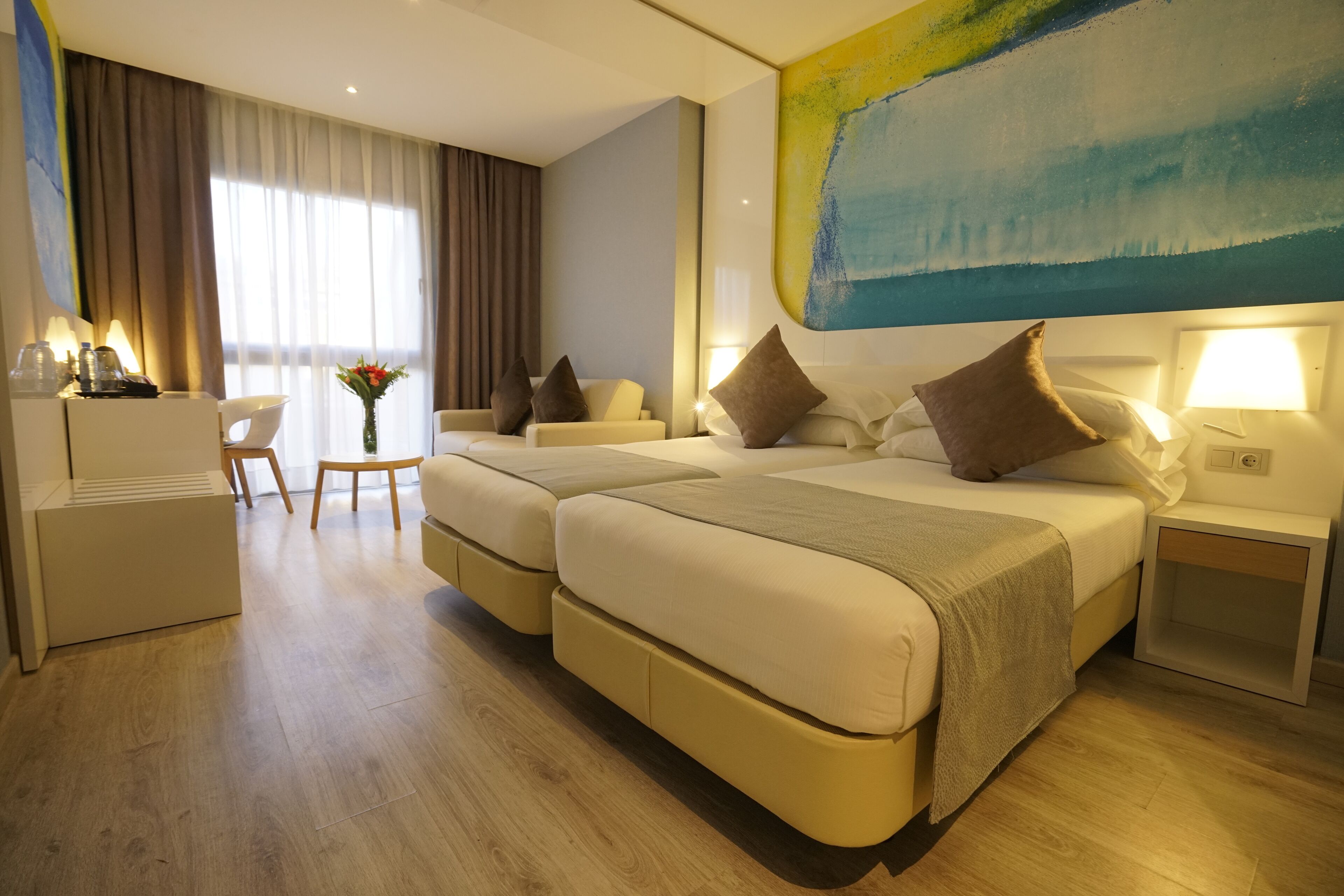 A hotel room with two beds, a desk, a chair, and a large abstract painting on the wall.