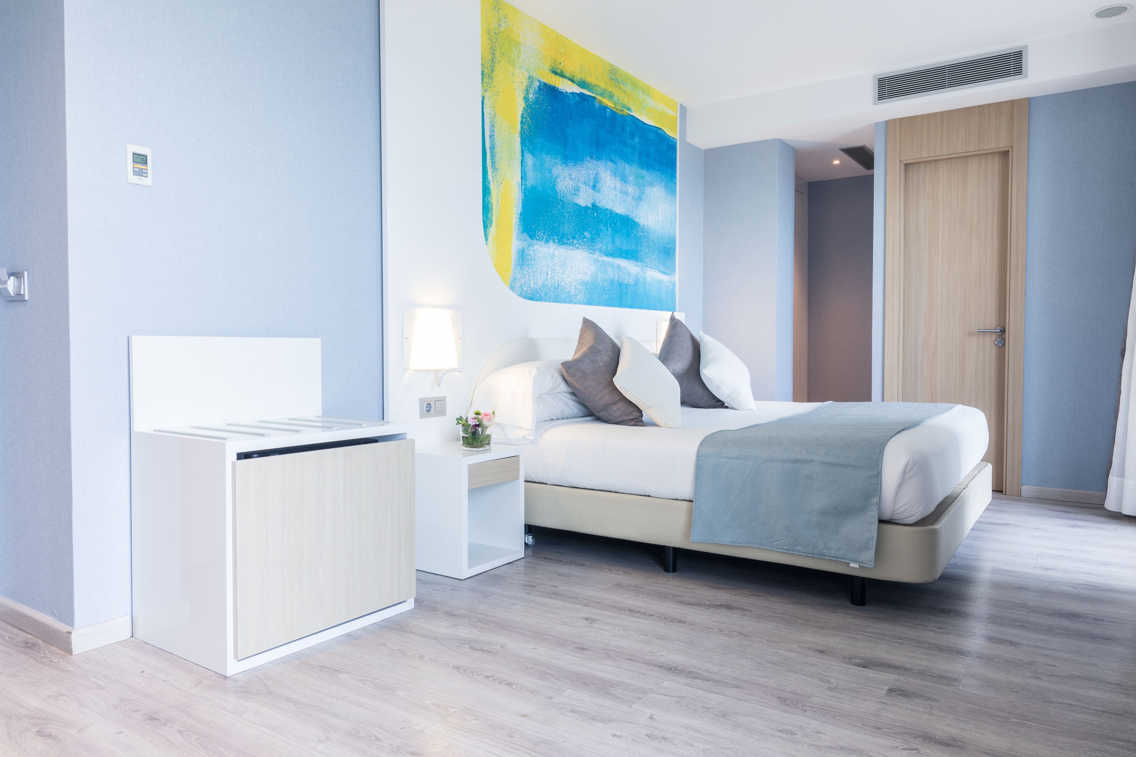 A modern bedroom with a bed, bedside tables, a nightstand, a wall art piece, and a door.