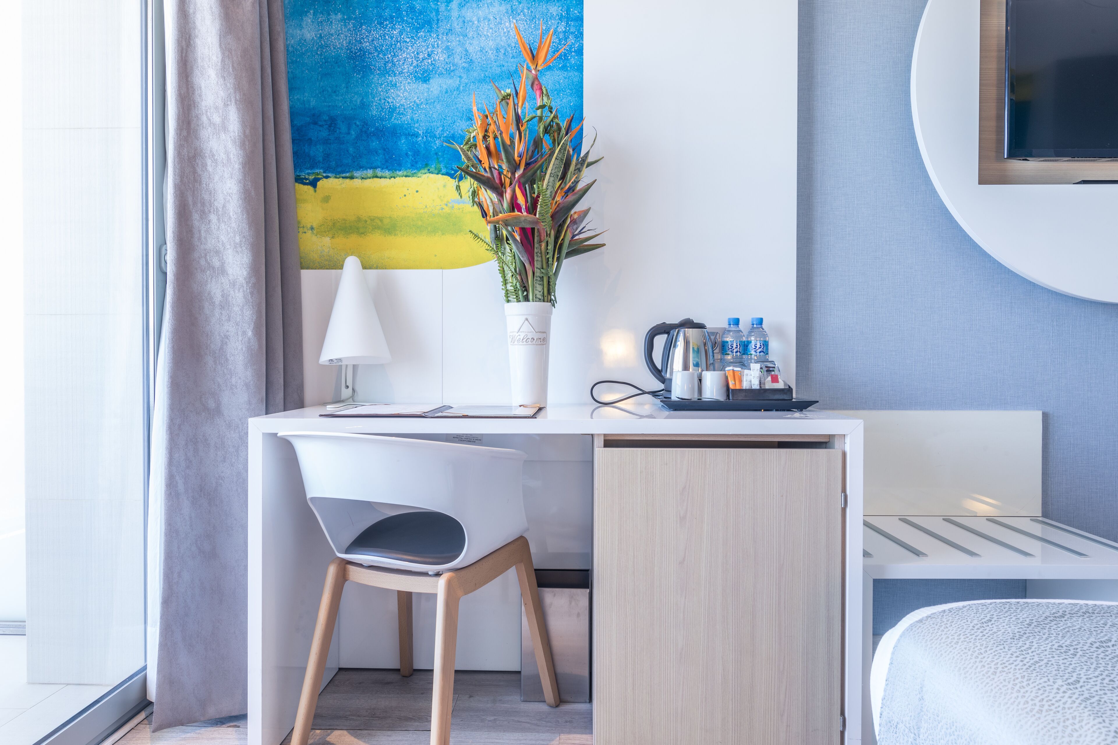 A modern hotel room with a desk, chair, and a large painting on the wall.