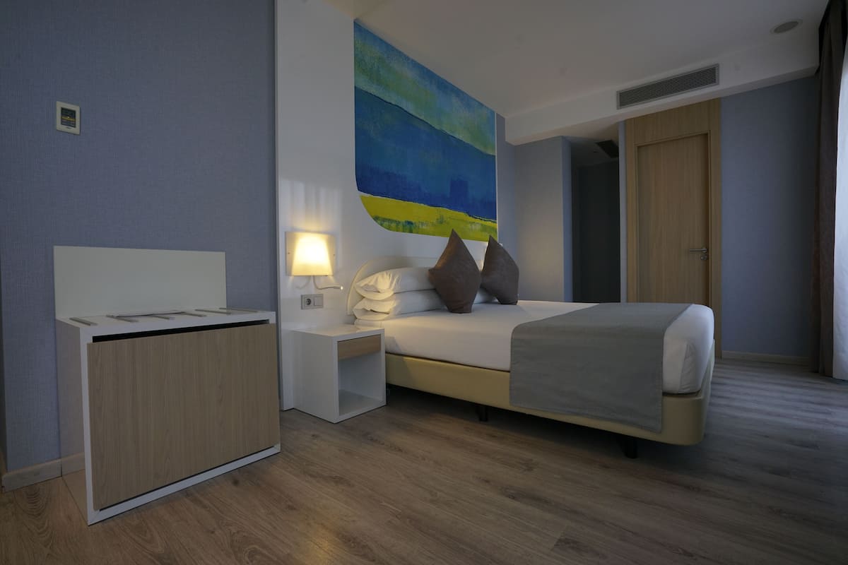Ein modernes Hotelzimmer mit Bett, Nachttisch, Lampe und einem Bild an der Wand.
