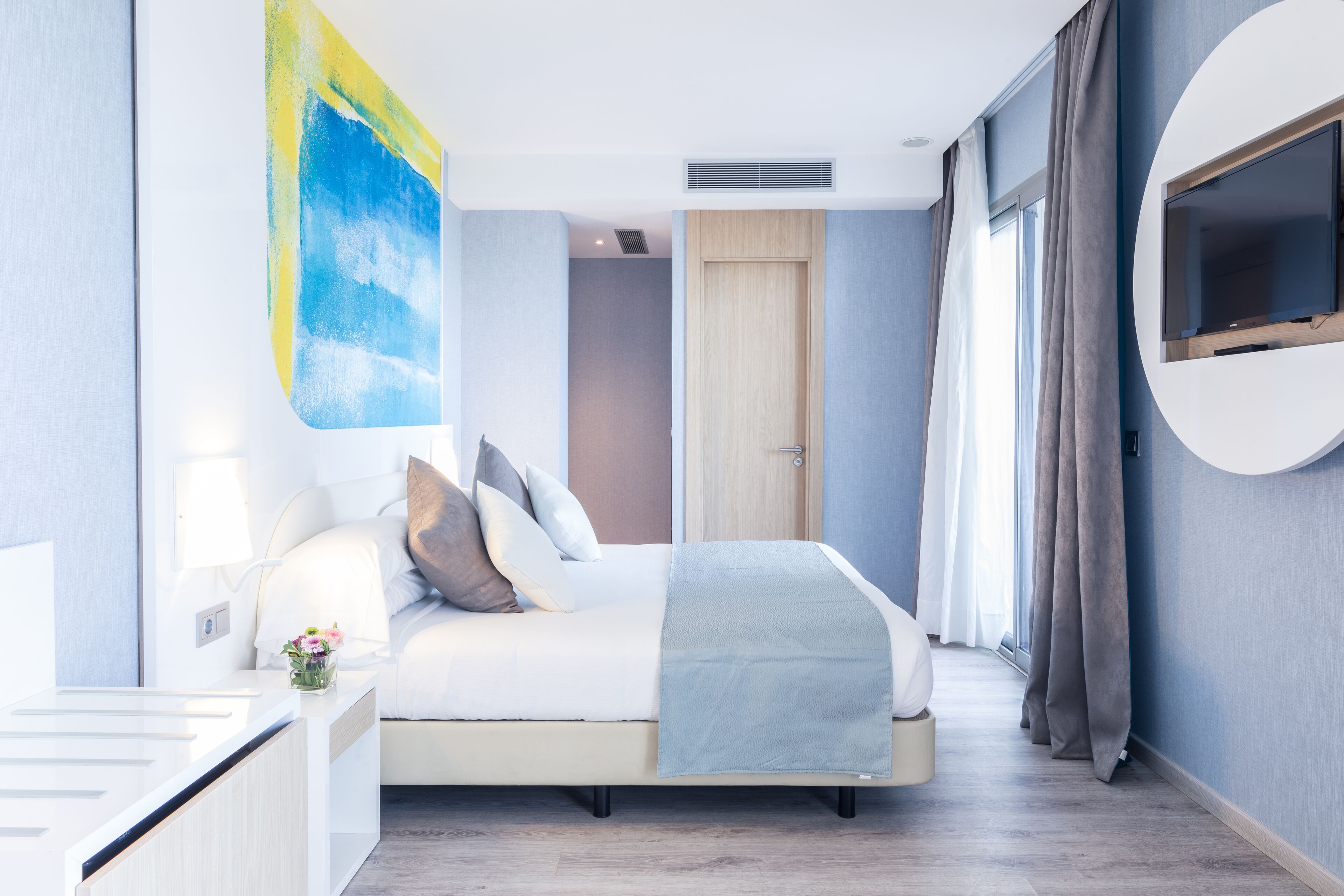 Ett modernt hotellrum med en säng, ett sängbord och ett stort fönster.