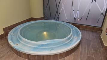 A hot tub in a room with tiled flooring and a decorative wall.