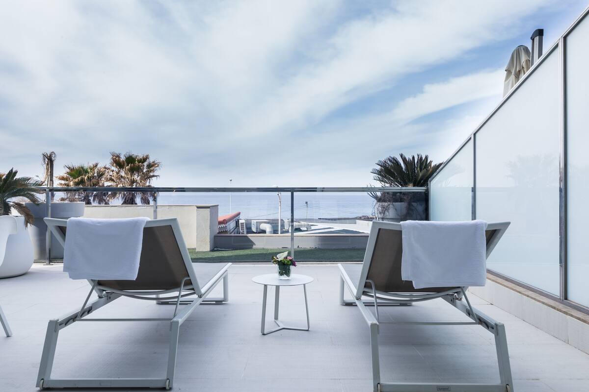 Eine Dachterrasse mit zwei Liegestühlen, einem kleinen Tisch und einem Blumentopf.