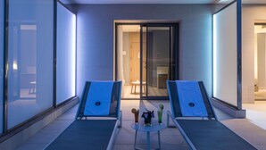 Une chambre d’hôtel moderne avec deux fauteuils, une petite table avec des boissons et une vue sur l’intérieur par une porte vitrée.
