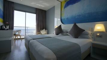 Habitación de hotel moderna con dos camas, un escritorio y un amplio ventanal con vista al mar.