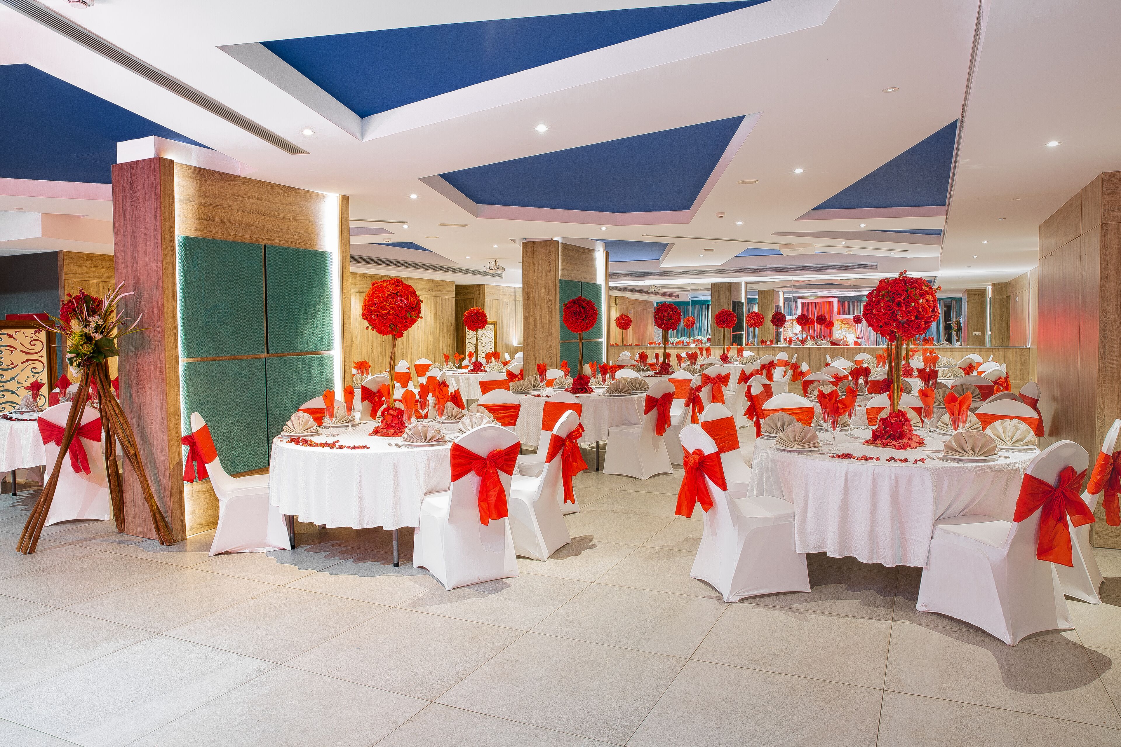 A banquet hall with round tables, white chairs, and red sashes.