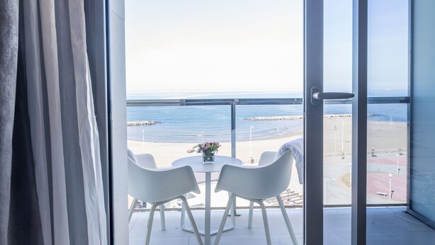 Un balcon avec une table et des chaises donnant sur une plage et la mer.