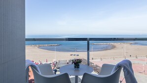 Un balcon donnant sur la plage, une table ornée d’un vase de fleurs et deux chaises.