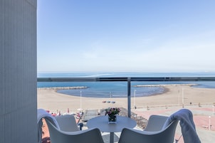 Un balcón con vista a la playa, una mesa con un jarrón de flores y dos sillas.